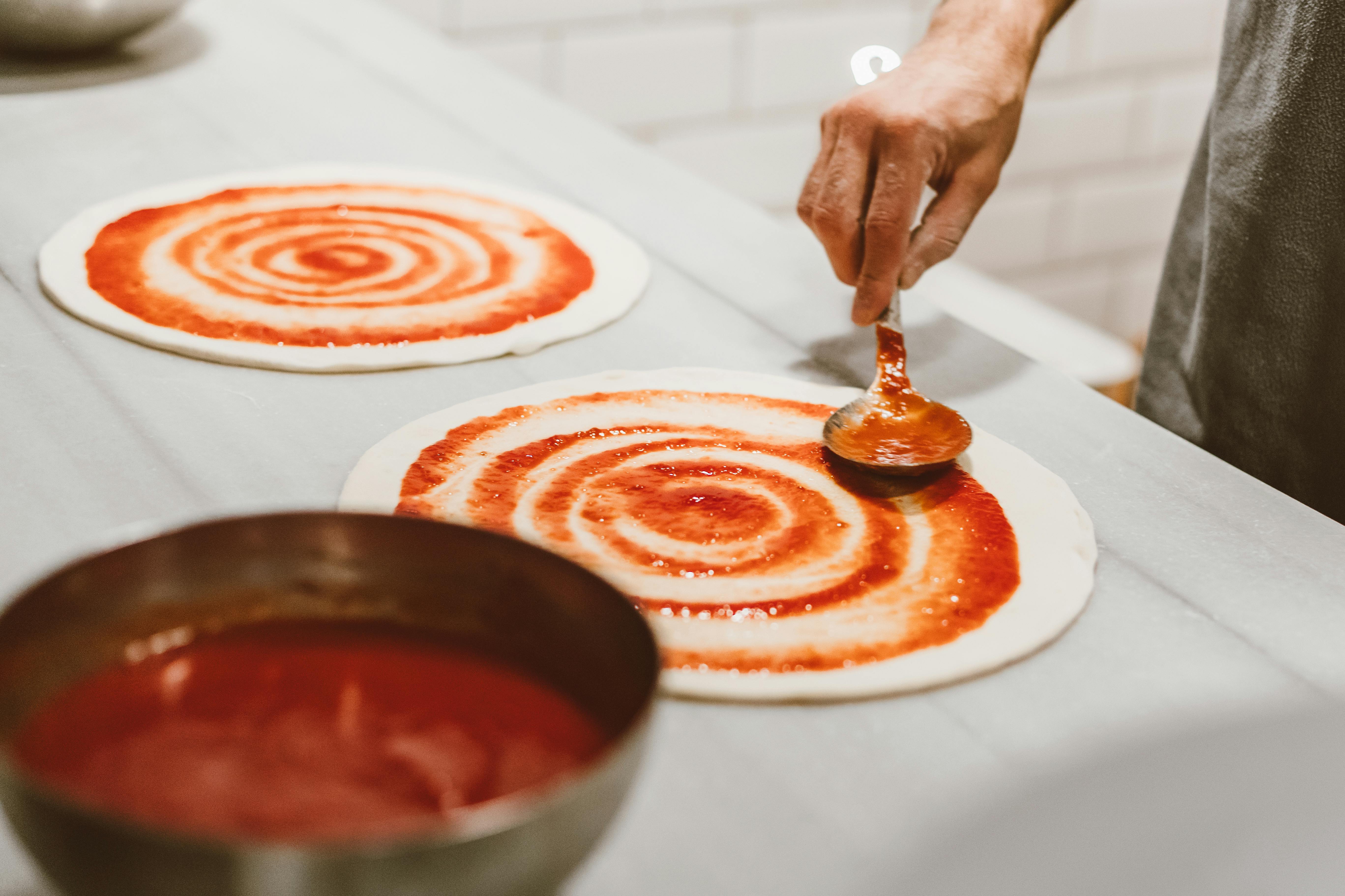 Chef spreading tomato sauce on pizza dough